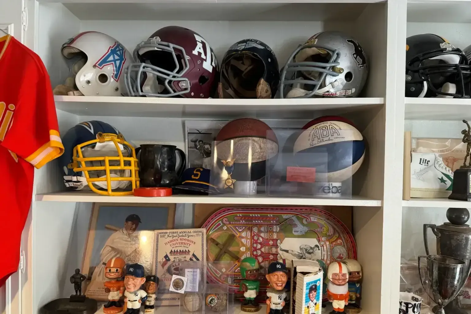 Sell signed baseballs — Shelf of vintage football helmets, ABA basketballs, bobbleheads and trophies beside a Chiefs jersey