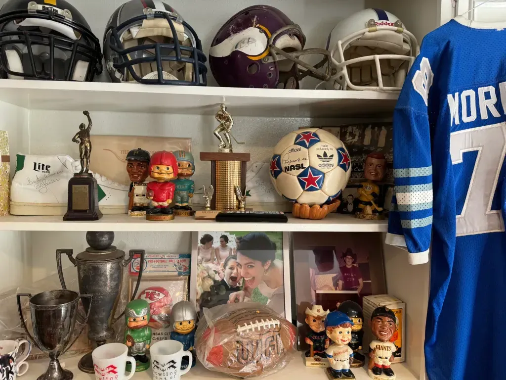Sell vintage sports memorabilia in San Antonio Tx — Shelf of vintage football helmets, an NASL soccer ball, bobbleheads, trophies and silver loving cups